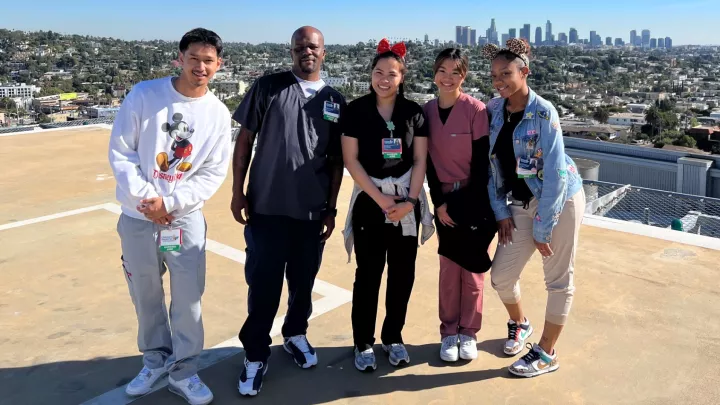 Five casually dressed nurse trainees stand on CHLA's helipad with the Los Angeles skyline in the background