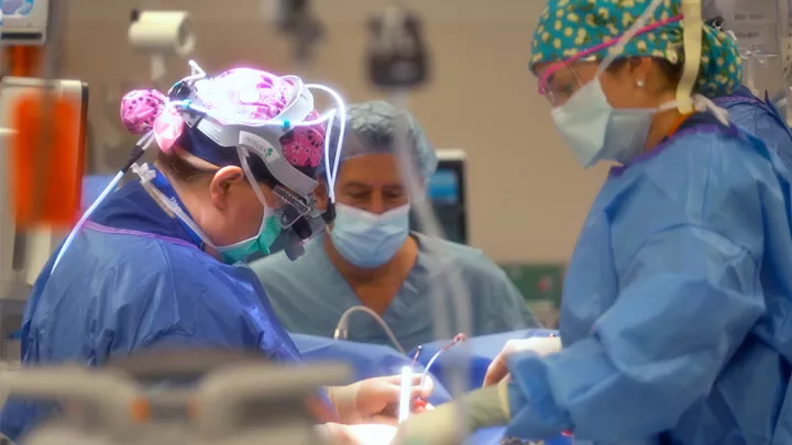 Masked surgeons wearing full PPE work on a patient in a hospital operating room