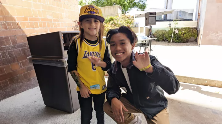Young boy with medium skin tone, long brown hair and a hand difference smiles as he poses with teenage boy with medium skin tone and dark hair and a hand difference