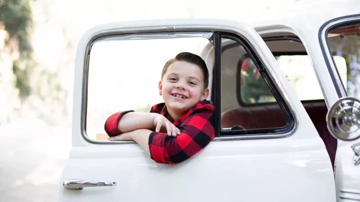 Young boy with light skin tone smiles as he looks out of the window of a white pickup truck