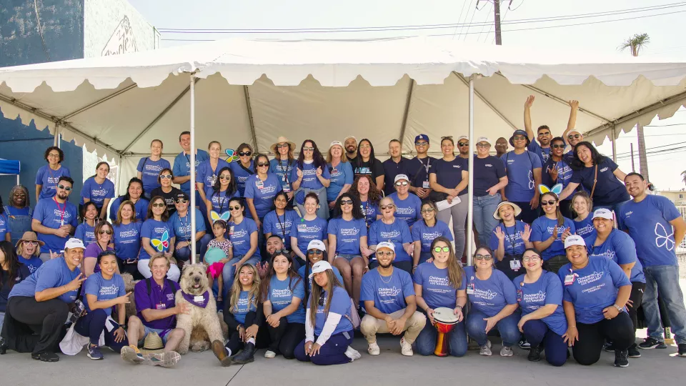 Approximately 60 CHLA team members wearing blue t-shirts pose beneath large canopy at the Community Wellness Festival