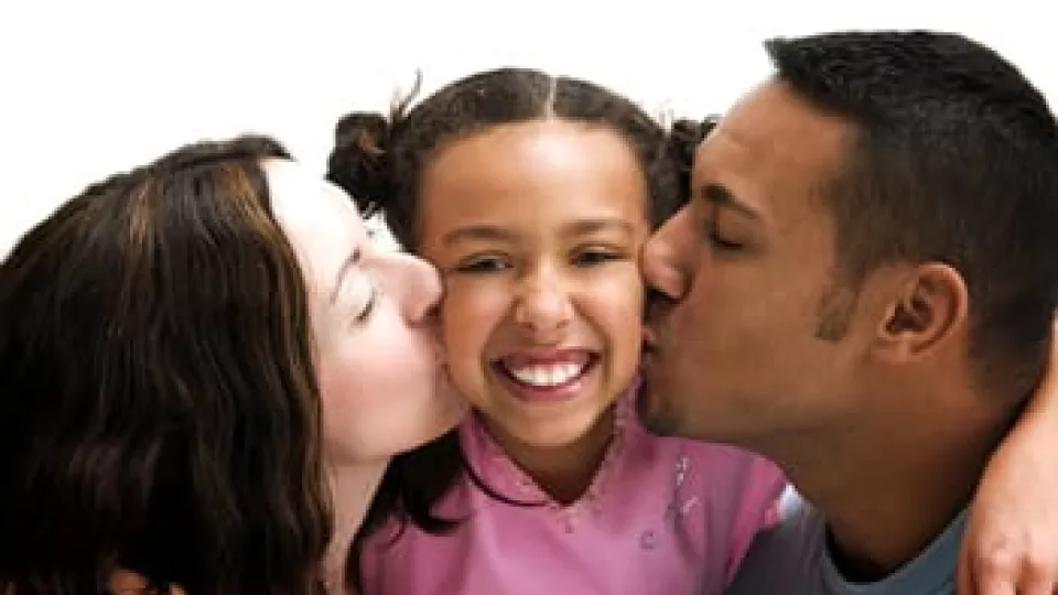 Parents kiss their daughter.