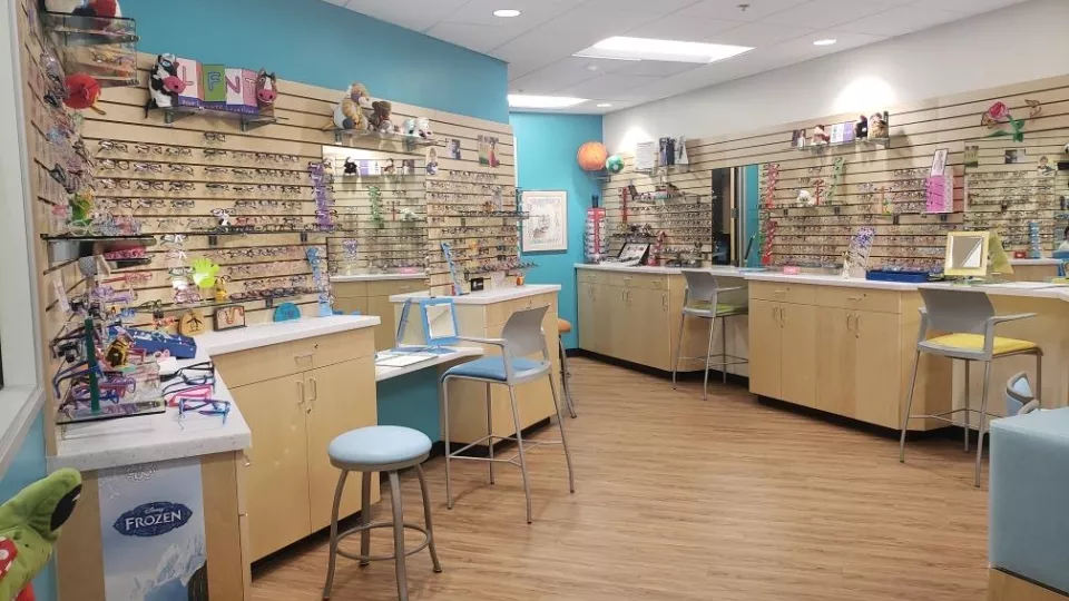 A colorful room with work stations and chairs, and walls lined with different types of children's eye glasses