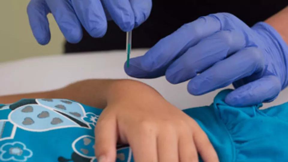 Close up of hands in surgical gloves applying an acupuncture needle to a child's wrist 