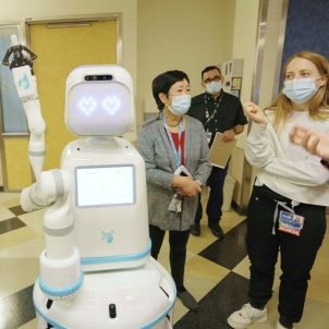 Moxi flashes heart-shaped digital eyes as it poses with CHLA’s Chief Pharmacy Officer Carol Takemoto and others