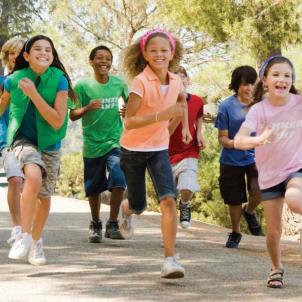 A diverse group of children wearing shorts and T-shirts is smiling and running. 