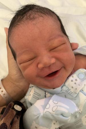 Close up of newborn with medium skin tone and dark hair smiles with their eyes closed