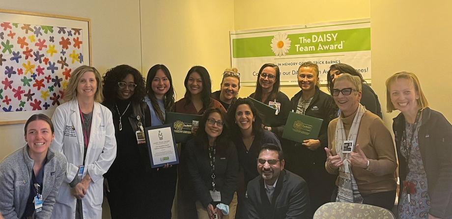 Group of 13 women and one man smile as they pose in office conference room with DAISY Team Award