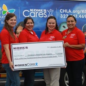 4 women in red shirts with the CHLA logo stand smiling and holding a large check, which is from Kohl's to Children's Hospital Los Angeles.