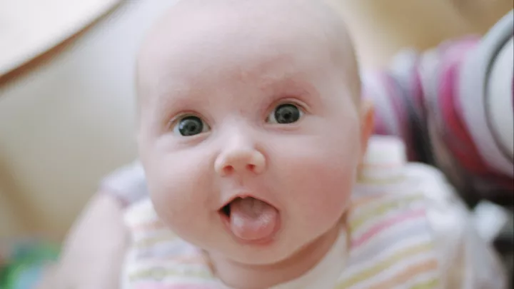 A baby with light skin tone sticks their tongue out.