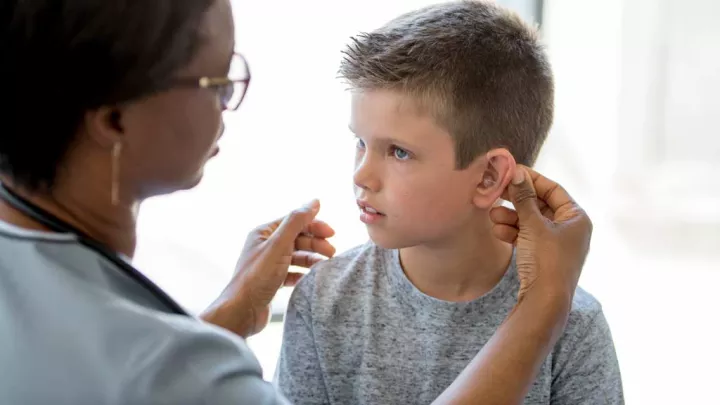 Physician with dark skin tone examines ear of young patient with light skin tone