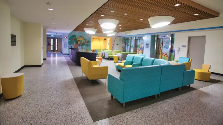 A colorful waiting room with teal and yellow furniture, playful wall art and bright lights.