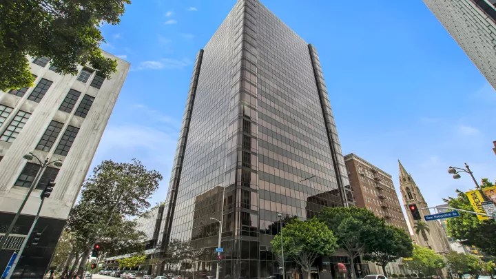 A street-level view of a tall, glass-covered building on a tree-lined urban street