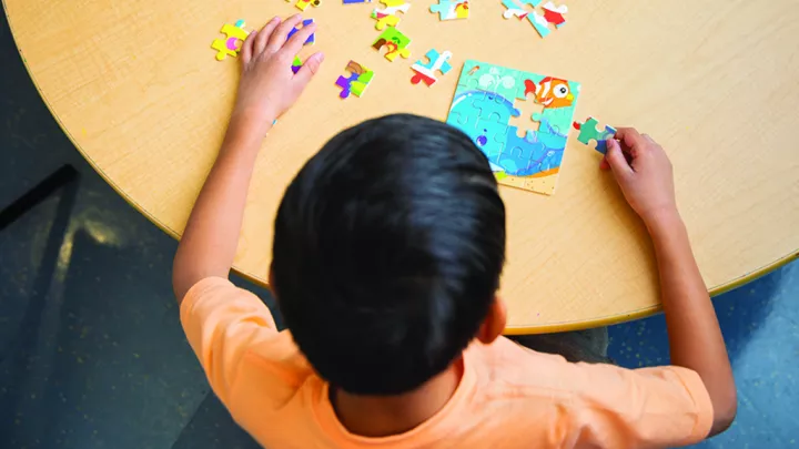 Young boy works on a brightly colored jigsaw puzzle of a fanciful underwater scene