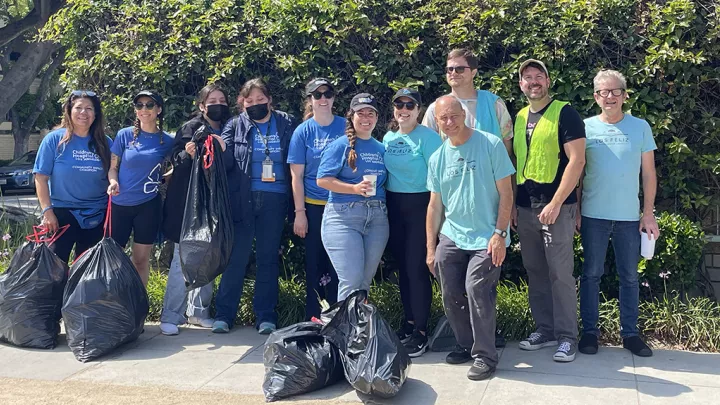 11 casually dressed members of CHLA’s Community Impact Champions Network volunteer team pose with full trash bags following beautification event