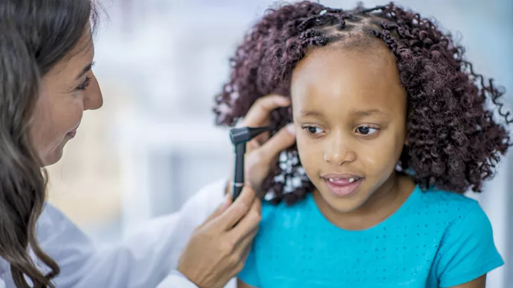 A female doctor with medium skin tone performs ear examination on a young girl with medium skin tone