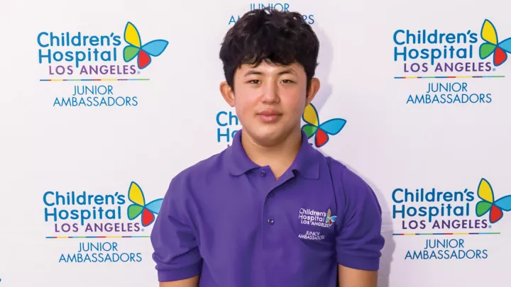 Teenager with light skin tone and dark hair stands against a CHLA background