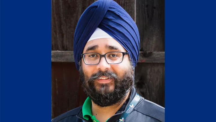 Headshot of a bearded man with medium skin tone wearing black glasses and a blue turban