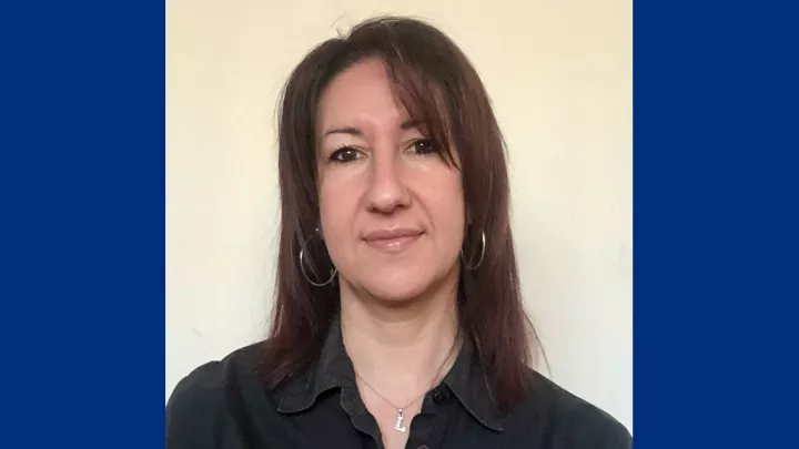 Headshot of a woman with light skin tone and brown shoulder-length hair wearing a black blouse against a neutral background