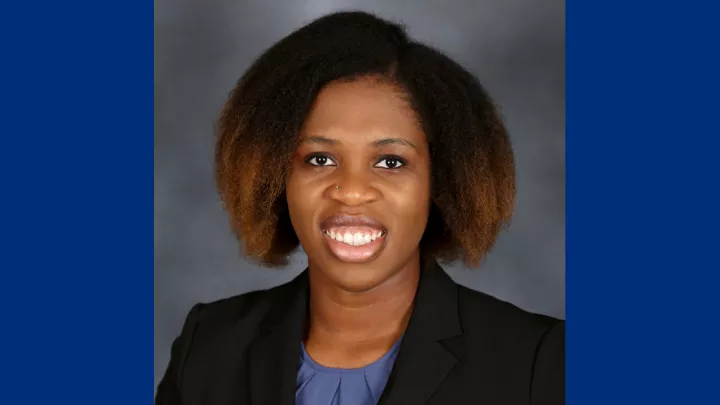 Headshot of a smiling woman with dark skin tone and dark hair wearing a blue blouse and dark suit jacket against a neutral indoor background