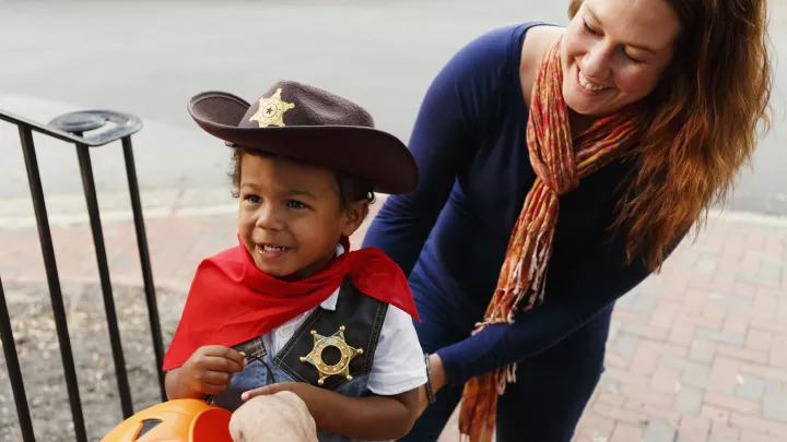Young boy dressed as a cowboy goes trick or treating with his mother