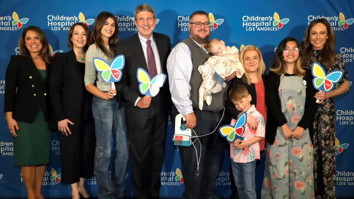 Hospital dignitaries, actresses and patient families smile as the pose with colorful hand-held Children's Hospital Los Angeles butterfly logos in front of a blue CHLA backdrop