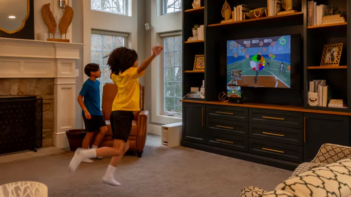 A boy leaps in the air as he starts to kick his leg in front of a TV screen, which shows a boy avatar kicking a large ball.