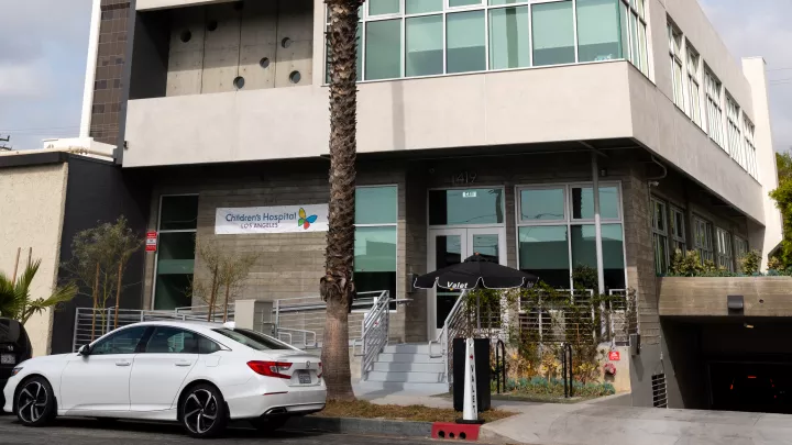 A white care is parked in front of a two-story office building with a banner that reads Children's Hospital Los Angeles
