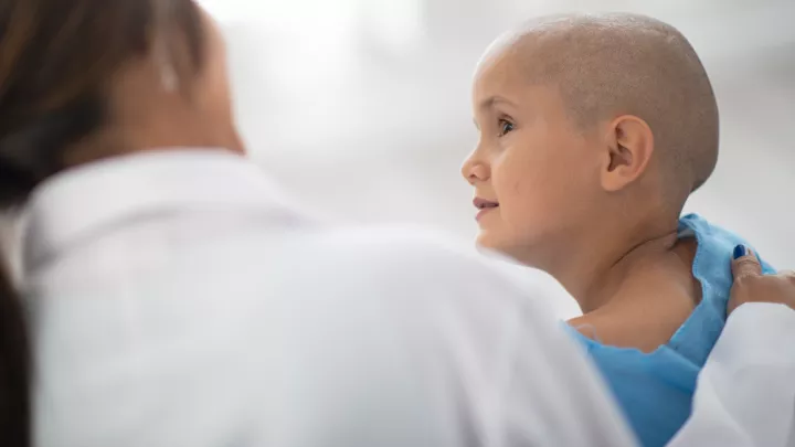 Young cancer patient with medium skin tone and shaved head and doctor seen from back