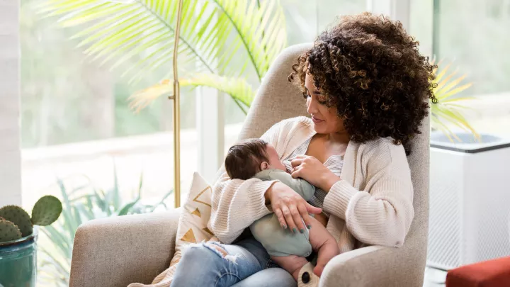A mother breastfeeds her newborn at home. 