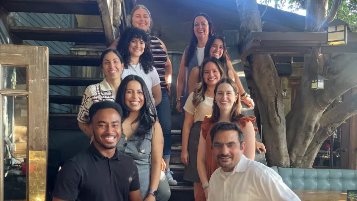 A group of adults with various skin tones wearing professional attire pose together on a staircase in an outdoor courtyard space.