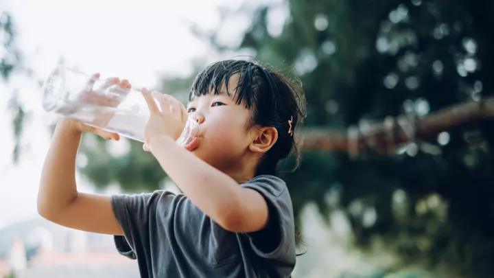 A child with medium light skin tone drinking from a large plastic water bottle.