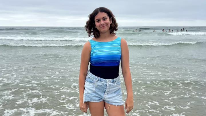 A smiling girl at the beach stand shin deep in ocean water.