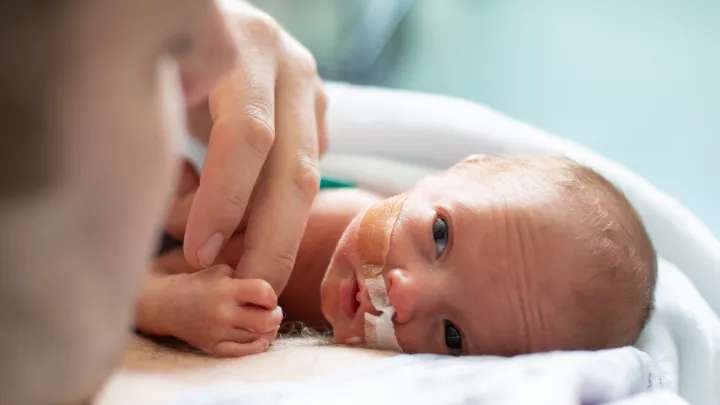 Light skin preemie with eyes open lies flat on side while watched by adult