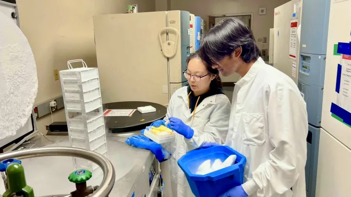 Dark haired woman on left, dark haired student on right with blue bucket