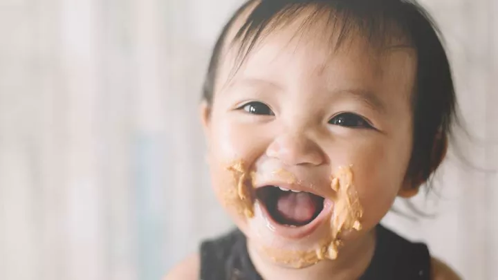 Happy smiling baby with peanutbutter on their cheeks.