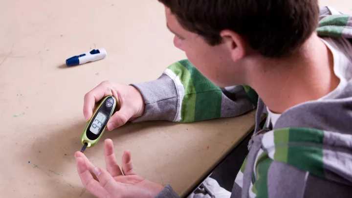 Teenage boy with type 2 diabetes performing a finger stick blood sugar test