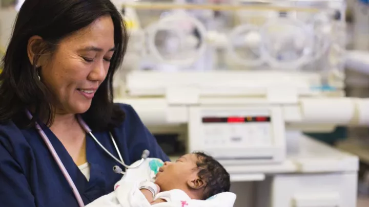 Female nurse smiling and holding newborn in neonatal intensive care unit