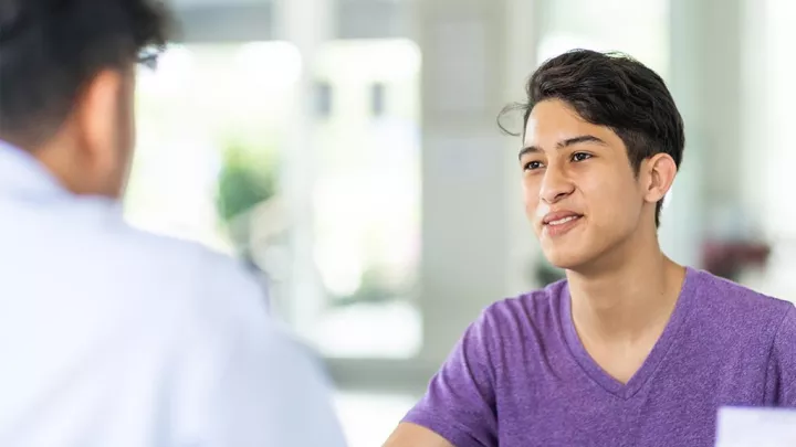 Patient with medium skin tone and dark hair speaks to health care provider in white lab coat