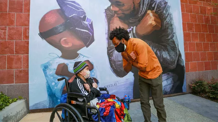 Daniel sitting in wheelchair and Nikkolas Smith in front of King Chad Mural at CHLA