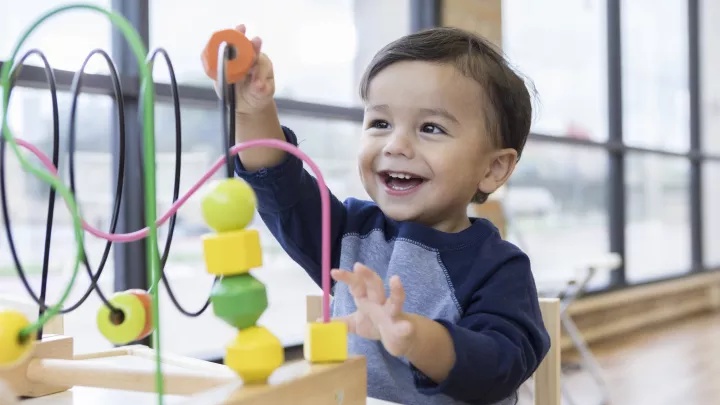 Smiling toddler with blue shirt playing with a colorful toy.