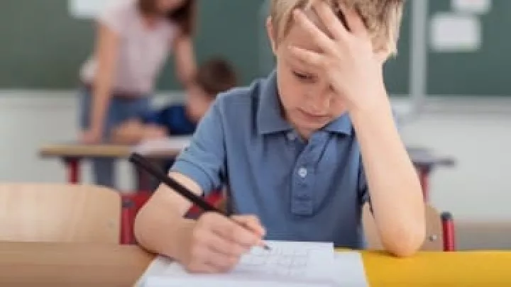 Young boy with light skin tone looks distressed as he works on a problem at school