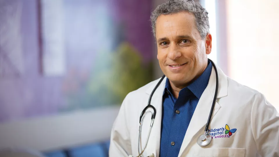 Guy Young, MD smiles in his lab coat with stethoscope draped around his neck