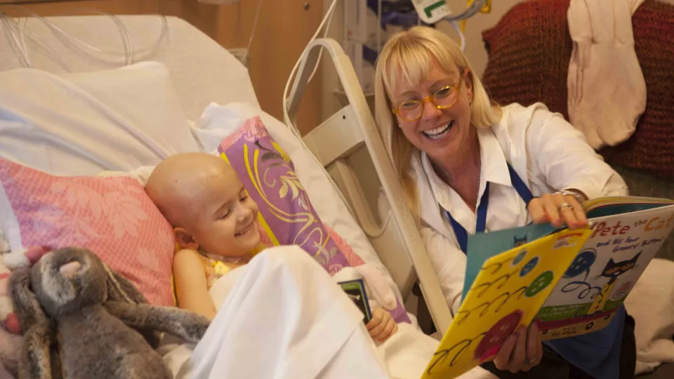 Nurse reading a children's book to a young child who is lying in a hospital bed.