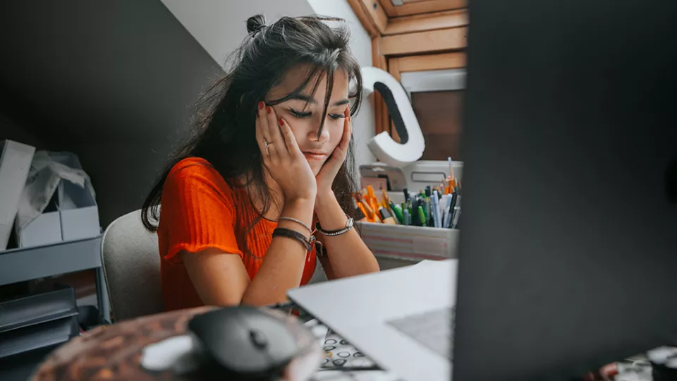 Female teenager looks stressed as she sits in front of her open laptop in her room