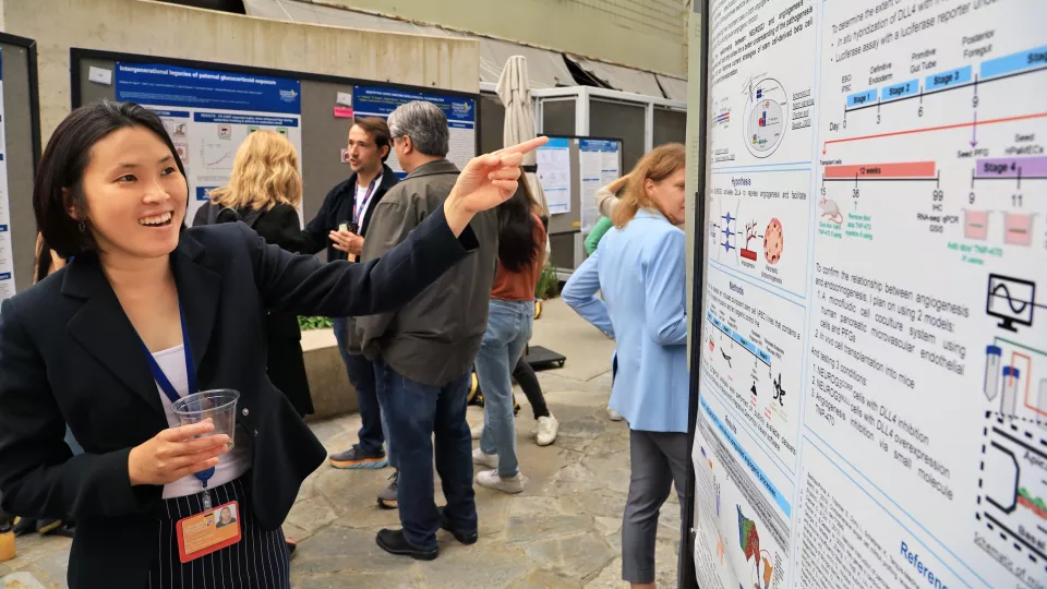 The Saban Research Institute graduate student Victoria Wang smiles and points at Science Day poster displaying her research