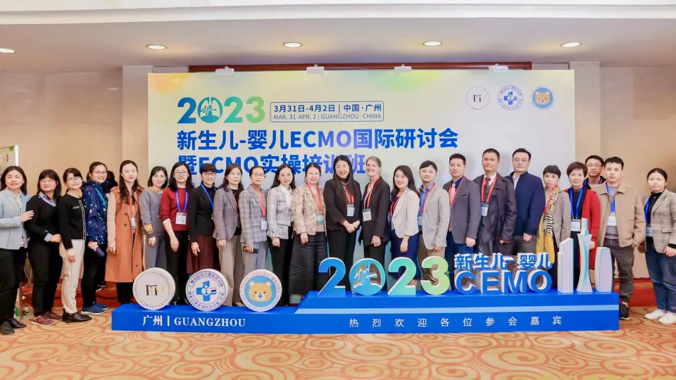 Rachel Chapman, MD, stands with 23 conference attendees in front of banner at the 2023 Guangzhou Newborn and Infant ECMO International Forum in Guangzhou, China