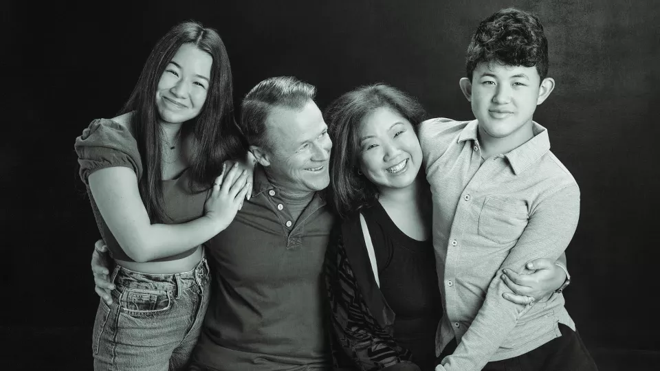 Casually dressed family of four smile as they pose for black and white family photo