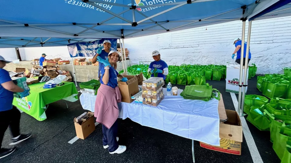 Volunteers wearing blue CHLA t-shirts stack food donations on foldable table underneath CHLA canopy
