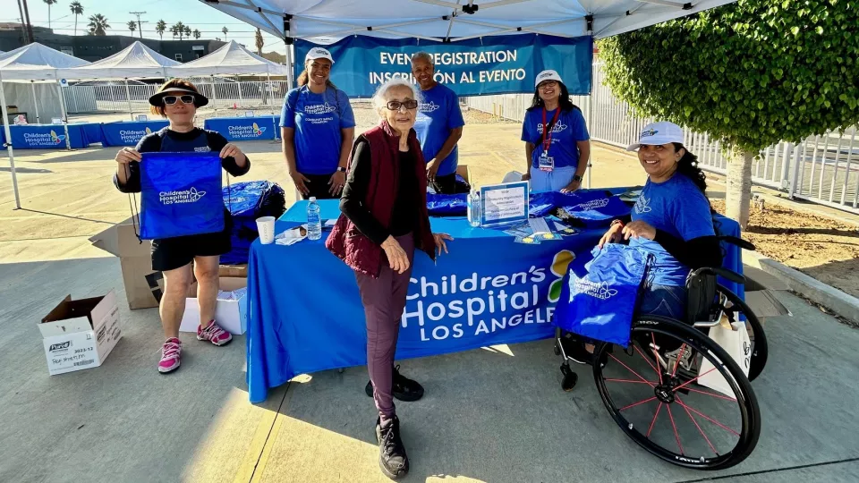 Volunteers wearing blue CHLA t-shirts stand beneath canopy at Community Wellness Festival